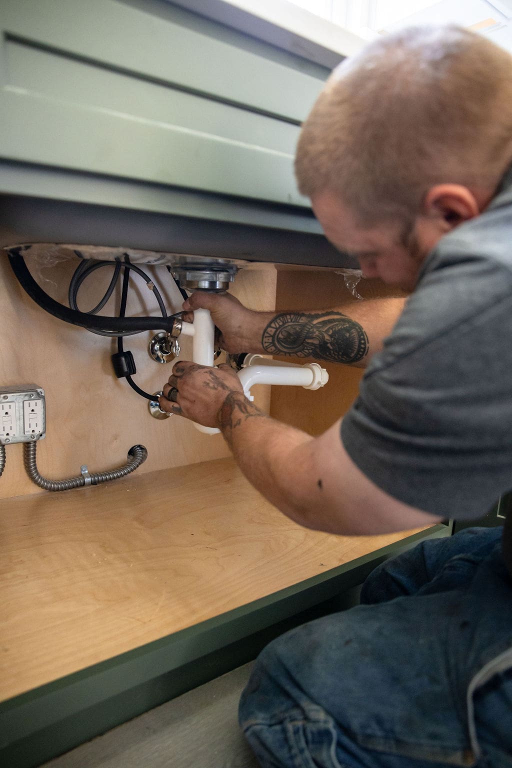 A plumber working on pipes under a sink